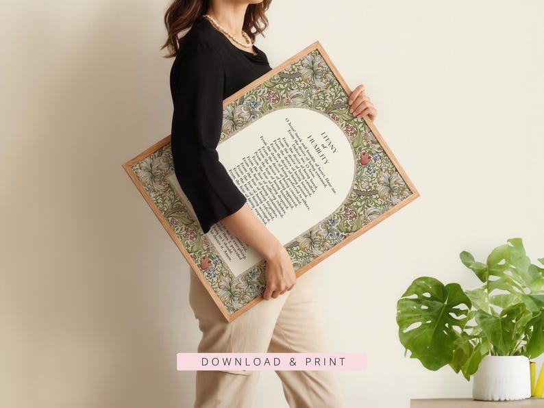 May include: A rectangular framed print featuring the Litany of Humility in black text centred on a white background. The border displays a detailed floral and botanical pattern in shades of green, red, and blue. The frame is a light-toned wood.