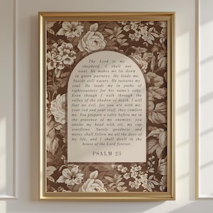 Puede incluir: Impresión enmarcada con el texto del Salmo 23 en forma de arco, sobre un fondo floral en tonos marrón y crema. El marco dorado añade un toque clásico a esta decoración mural religiosa.