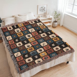 May include: A patterned throw blanket featuring a repeating design of multi-coloured hexagonal shapes. Each hexagon contains a different graphic, including skulls and flames. The blanket has a fringed edge. The colours include black, brown, blue, and yellow.