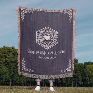 May include: A navy blue throw blanket featuring a white geometric design, the names "Samantha & David", and the date "July 30th, 2025". The blanket has a fringed edge and floral corner accents.