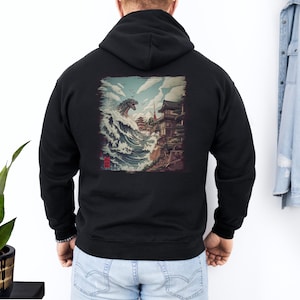 May include: Black hooded sweatshirt featuring a graphic print of a monster emerging from a wave in front of a Japanese temple.