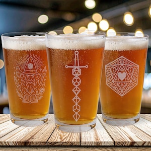 May include: Three pint glasses filled with beer, each etched with a different design. One glass features a wizard, another a sword and dice, and the third a geometric heart design. The glasses are on a wooden table.