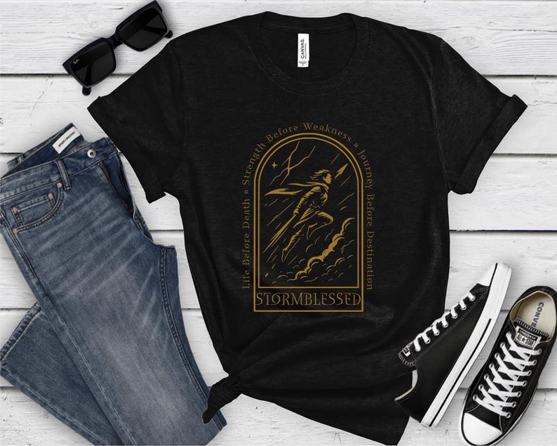 Puede incluir: Camiseta negra con un gr&aacute;fico dorado de una figura corriendo a trav&eacute;s de una tormenta, con el texto "Life Before Death = Strength Before Weakness = Journey Before Destination" y "Stormblessed". Incluye vaqueros azules, gafas de sol negras y zapatillas negras.