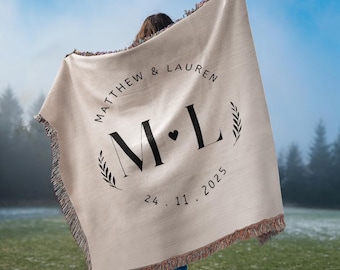 May include: Beige woven throw blanket with black text and fringe. The blanket features the names "MATTHEW & LAUREN" in a circle, with "M L" and a heart in the center, and the date "24.11.2025" below. The blanket is held up outdoors.