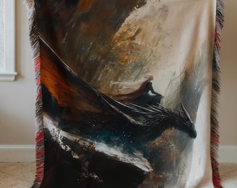 Peut inclure: Une couverture en tissu tissé avec un motif de fantasy représentant une femme chevauchant un dragon noir dans une forêt. La femme porte une robe blanche et une cape rouge. Le dragon vole à travers une forêt brumeuse avec une falaise rocheuse sombre en arrière-plan.