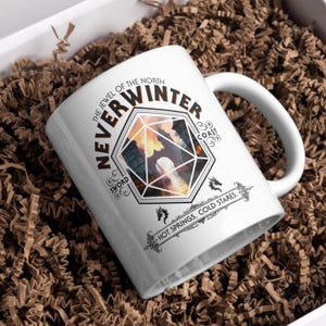 May include: White ceramic mug with a graphic design featuring a stylized image of a city skyline inside a 20-sided die. The text "The Jewel of the North Neverwinter Sword Coast Hot Springs, Cold Stares." is printed around the die.