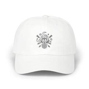 Könnte beinhalten: Eine weiße Baseballkappe mit einem schwarzen Grafikdesign. Das Design umfasst einen Mond, Sterne, Pfeile, eine Axt und andere himmlische und natürliche Elemente. Die Kappe hat einen gebogenen Schirm und eine runde Krone.