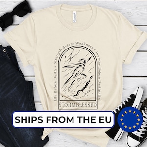 Könnte beinhalten: Cremefarbenes T-Shirt mit einer schwarzen Grafik einer Figur, die durch einen Sturm rennt, mit dem Wort "STORMBLESSED" darunter. Das Shirt zeigt auch die Sätze "Life Before Death = Strength Before Weakness" und "Journey Before Destination".