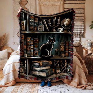 Puede incluir: Un gato negro se sienta en un estante lleno de libros, velas y otros objetos mágicos. El estante es parte de un tapiz con un fondo azul oscuro y flecos rojos.