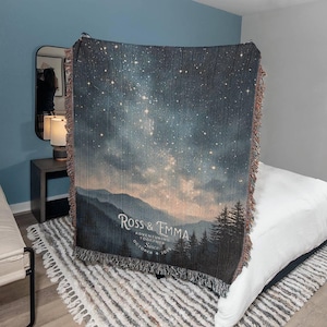 May include: A woven throw blanket with a night sky design, mountains, and trees. The blanket has a fringed edge and the text "Ross & Emma Adventuring Together Since October 4, 2023". The blanket is suitable for a double bed.