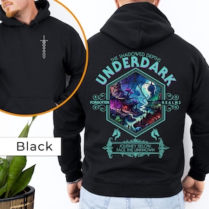 May include: Black hooded sweatshirt with a graphic print of a Dungeons and Dragons themed design. The design features a large, multi-colored, hexagonal die with the words "The Shadowed Depths Underdark Forgotten Realms" and "Journey Below Face The Unknown" printed around it.