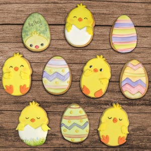 May include: Assortment of Easter biscuits decorated with chicks and eggs. The biscuits are yellow, white, green, purple, and pink. Some biscuits have the word "hello" written on them.