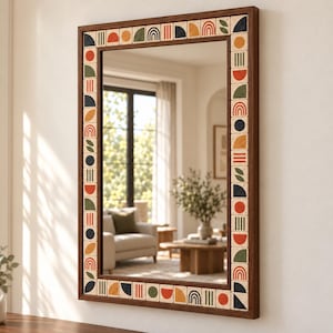 Könnte beinhalten: Ein rechteckiger Wandspiegel mit einem dunkelbraunen Holzrahmen. Der innere Rand ist mit einer Reihe quadratischer Fliesen verziert, die verschiedene geometrische Muster wie Kreise, Halbkreise, Bögen und Linien in Orange, Grün und Marineblau zeigen.