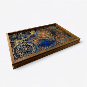 Puede incluir: Una bandeja rectangular de madera con un diseño decorativo. El interior de la bandeja presenta un fondo azul con patrones circulares dorados y naranjas. El marco de madera es de color marrón medio y la bandeja está vacía.