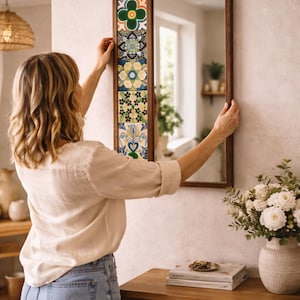 Pode incluir: Um espelho retangular com moldura de madeira e azulejos decorativos. Os azulejos apresentam padrões florais e geométricos em tons de verde, azul e amarelo. O espelho está pendurado numa parede clara.