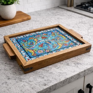 Puede incluir: Bandeja de madera rectangular con diseño floral. La bandeja tiene un marco y asas de madera marrón claro. El centro de la bandeja presenta un fondo azul con un vibrante estampado floral en rojo, amarillo y verde.