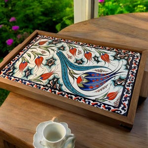 Puede incluir: Una bandeja de servir de madera con un inserto de cerámica pintada a mano. La baldosa presenta un diseño floral con tulipanes azules, rojos y verdes sobre un fondo blanco.