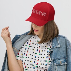 May include: Red baseball cap with white embroidered text that reads "The Leopards Are Eating Your Face".
