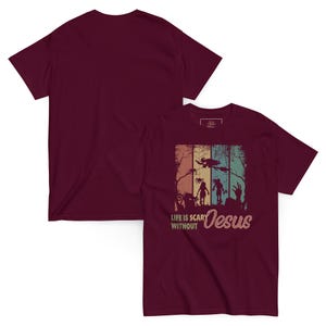May include: Maroon t-shirt featuring a graphic with the text "Life is Scary Without Jesus." The design includes silhouettes of zombies, a witch, and a spooky forest scene in a retro color palette. The back of the shirt is plain.
