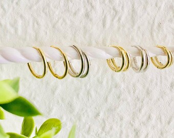 Puede incluir: Un conjunto de aros de oro y plata de varios tamaños colgados de una cuerda blanca. Los aros son todos simples y elegantes.