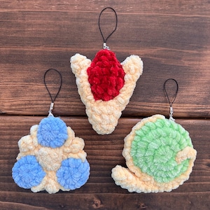 May include: Three handmade crochet charms in the image. One is a light yellow with blue accents, another is a light yellow with a red center, and the third is a light yellow with a green spiral. Each charm has a black loop for hanging.