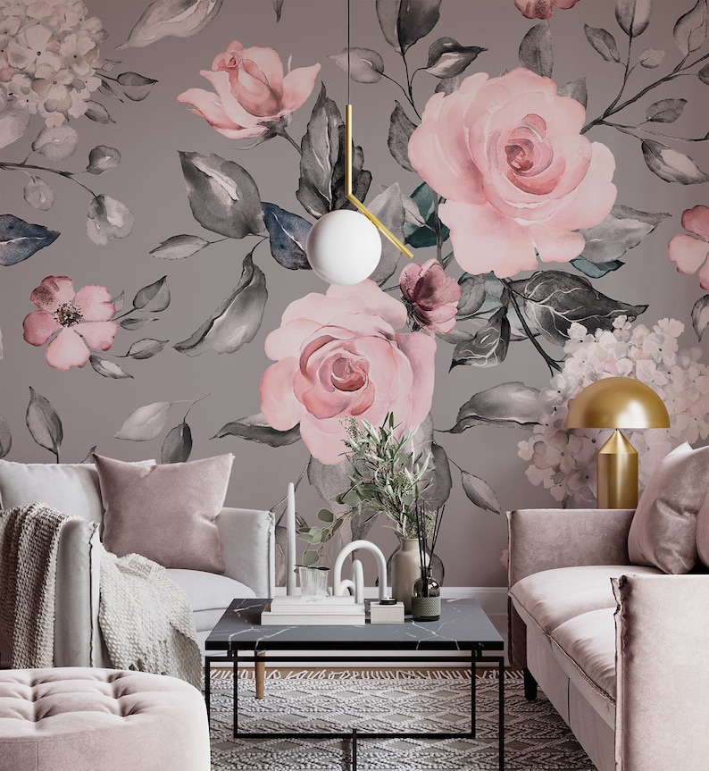 May include: A living room interior with a gray wall featuring a floral wallpaper with pink roses and gray leaves. The room is decorated with a gray couch, a pink armchair, a coffee table, and a gold lamp.