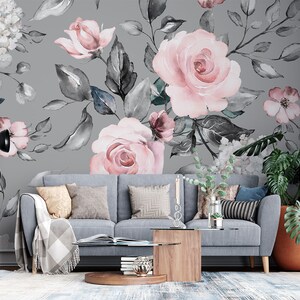 May include: A gray living room with a gray couch and a floral wallpaper featuring pink roses and gray leaves. A potted plant with large green leaves is in the corner of the room.