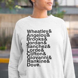 May include: White sweatshirt with black text listing names: Wheatley, Angelou, Brooks, Jordan, Sanchez, Lorde, Clifton, Giovanni, Rankine, and Dove. The sweatshirt is a crew neck style.