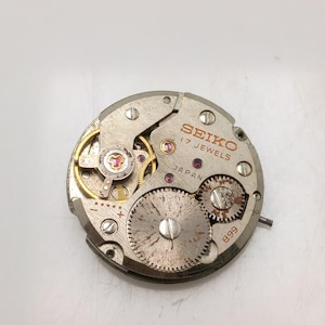 May include: A close-up of a Seiko watch movement. The silver-toned mechanism features multiple gears, jewels, and the text "SEIKO 17 JEWELS JAPAN" in red. The number "899" is also visible.
