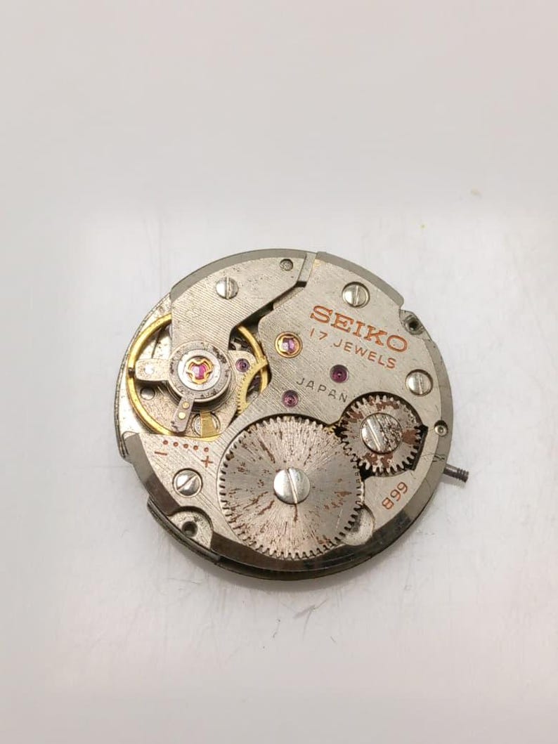 May include: A close-up of a Seiko watch movement. The silver-toned mechanism features multiple gears, jewels, and the text "SEIKO 17 JEWELS JAPAN" in red. The number "899" is also visible.