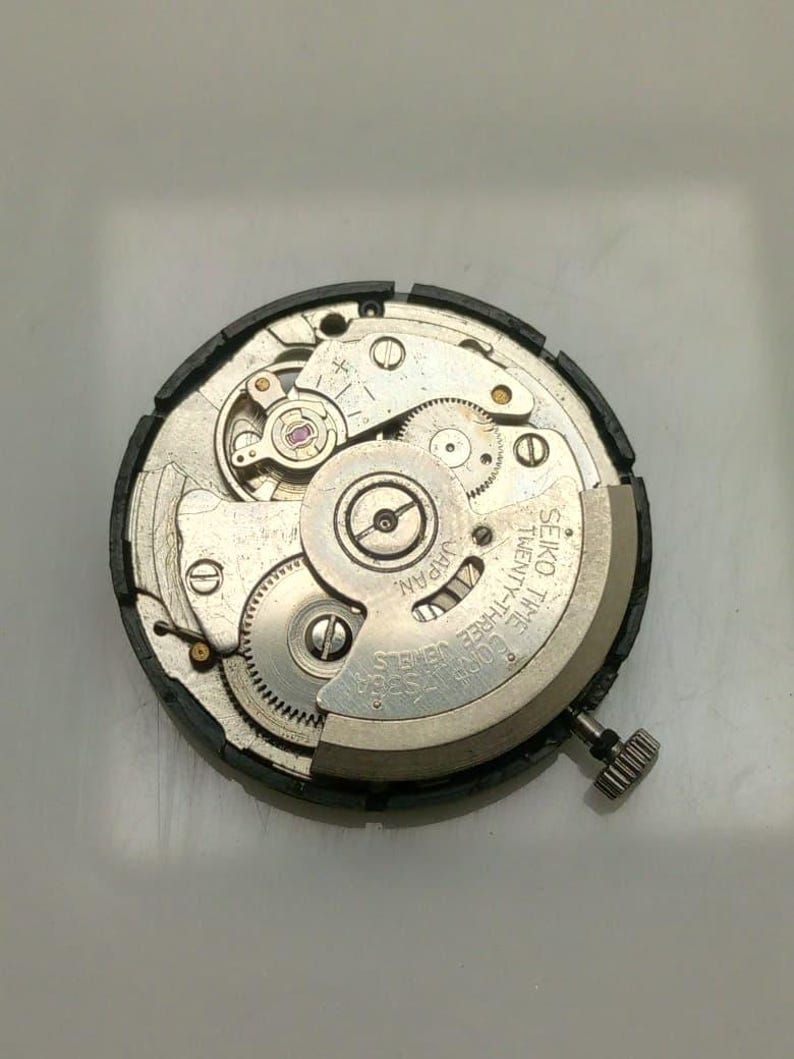 May include: Close-up of a Seiko watch movement, showcasing intricate gears, springs, and jewels. The silver-toned components are set against a dark background. The text "SEIKO TIME TWENTY-THREE JEWELS JAPAN" is visible.