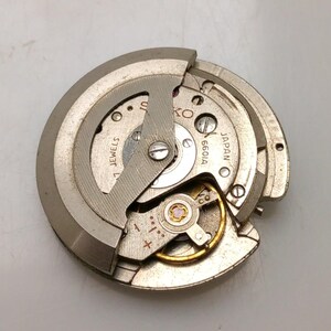 May include: A close-up of a Seiko watch movement, featuring intricate gears and components. The metal parts are silver and gold, with the text "SEIKO" and "JAPAN" visible. The movement is labeled "6601A" and "1 JEWELS".