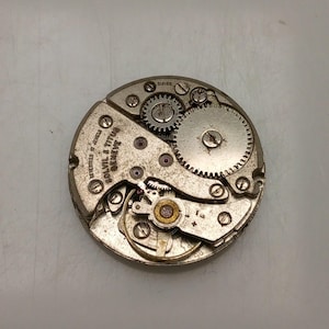 May include: Close-up of a vintage watch movement with gears, screws, and the text "SOLVIL & TITUS GENEVE". The watch mechanism is silver-toned with small red jewels and intricate details, showcasing the inner workings of a timepiece.
