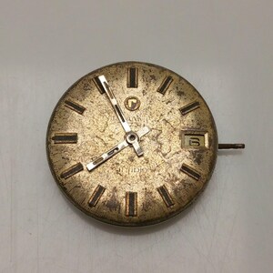 May include: A vintage watch face with a gold-toned, textured surface. The face features black rectangular hour markers, gold hands, and a date window displaying the number 6. The watch face has the brand name "AVIA" and "IDIO" printed on it.