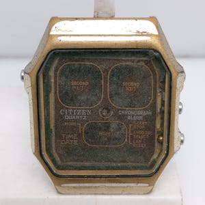 May include: A gold-toned Citizen Quartz watch with a digital display. The watch has a chronograph and alarm function. The watch face has the text "SECOND 1/10", "SECOND 10/1", "CITIZEN QUARTZ", "MODE", "TIME DATE", "MODE", "CHRONOGRAPH ALARM", "START. STOP", "1/100 SEC", "SELECT", "LAP", "RESET".