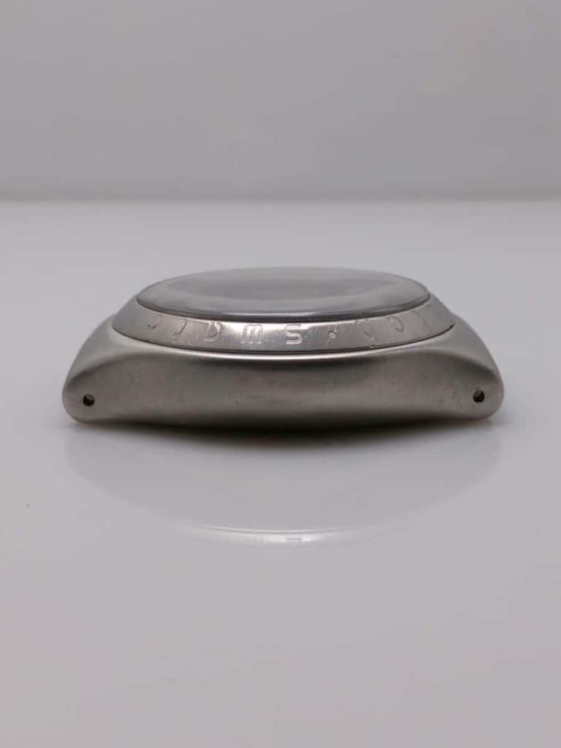 May include: A stainless steel wristwatch with a dark face and a curved, polished metal case. The watch has a circular face with a clear crystal and a bezel with engraved markings. The watch is shown from a side profile.