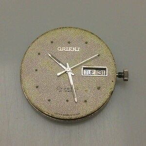 May include: A vintage Orient watch face with a textured, gold-toned dial. The watch face displays the Orient logo, the day and date (TUE 31), and silver hands. The watch has a crown and is marked "Crystal 21 Jewels" and "Japan Y46942274-G05".