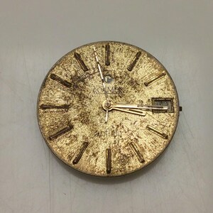 May include: A vintage gold-toned watch face with a textured surface. The watch face features gold-colored hour markers and hands. The brand name "ROAMER" is visible at the top. The watch face has a rectangular date window at the 3 o'clock position.