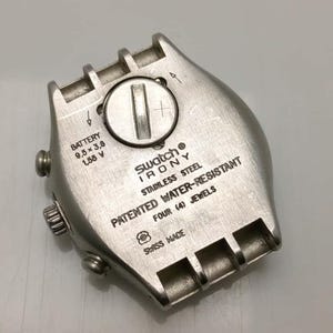 May include: A close-up of a Swatch Irony watch back. The stainless steel case features the text "PATENTED WATER-RESISTANT" and "FOUR (4) JEWELS". The watch back also includes the battery size: 9.5 x 3.6 mm, 1.55 V. Swiss made.