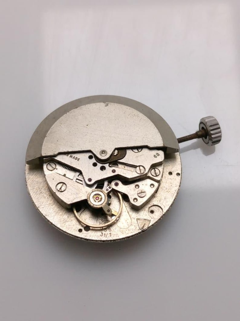 May include: A detailed close-up of a silver watch movement, showcasing intricate gears, screws, and a winding stem. The words "SWISS MADE" are visible. The circular mechanism is highly detailed.