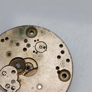 Pode incluir: Close-up de um movimento de rel&oacute;gio dourado com engrenagens vis&iacute;veis e a inscri&ccedil;&atilde;o "IWC" no lado.