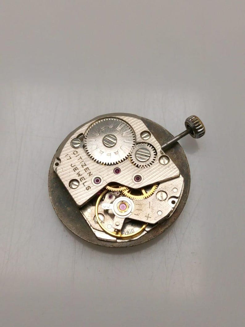 May include: Close-up of a Citizen watch movement with visible gears, jewels, and a winding stem. The silver-toned mechanism features the text "CITIZEN 17 JEWELS". The watch movement is a vintage item.