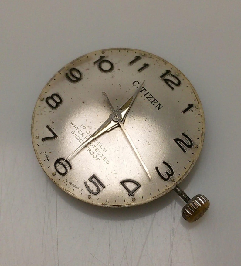 May include: A vintage Citizen watch face with a silver dial and black numerals. The watch face has gold-colored hands and the word "CITIZEN" is printed at the top. The text "17 JEWELS WATER PROTECTED SHOCK PROOF" is also visible.