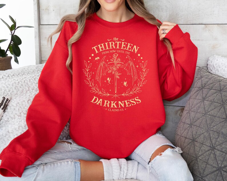 May include: Red sweatshirt with a gold graphic design featuring a sword, wings, and the text "the thirteen from now until the darkness claims us".