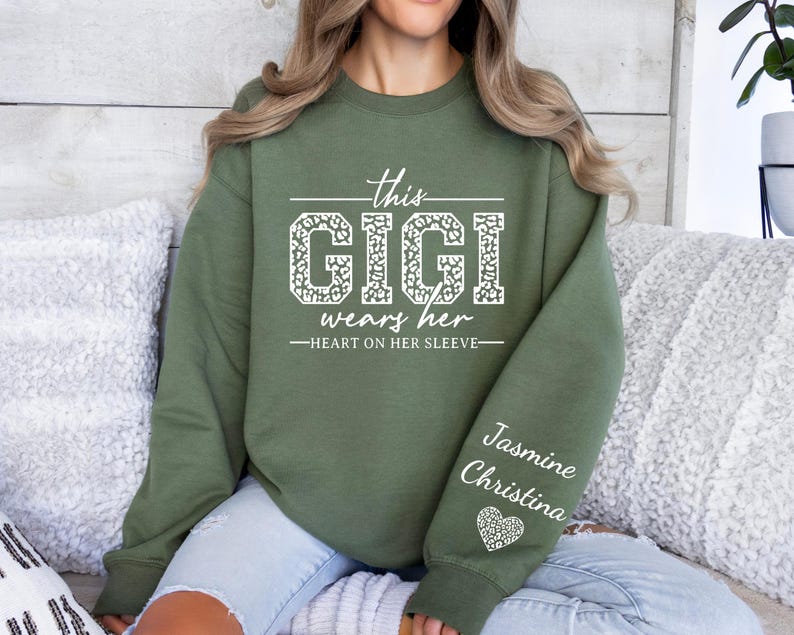 May include: Green sweatshirt with the text "This Gigi wears her heart on her sleeve" in white with a leopard print design. The sleeve has the names "Jasmine Christina" in white with a heart with a leopard print design.