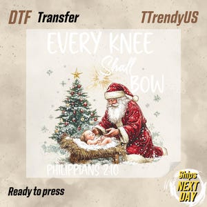 May include: DTF transfer featuring Santa Claus with a baby in a manger, a Christmas tree, and the text "EVERY KNEE SHALL BOW" and "PHILIPPIANS 2:10". The image has a watercolor style with a neutral background.