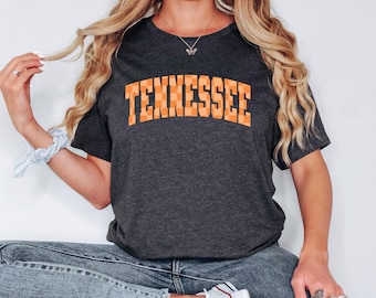May include: A dark gray t-shirt with the word "Tennessee" printed in orange and white checkered letters.