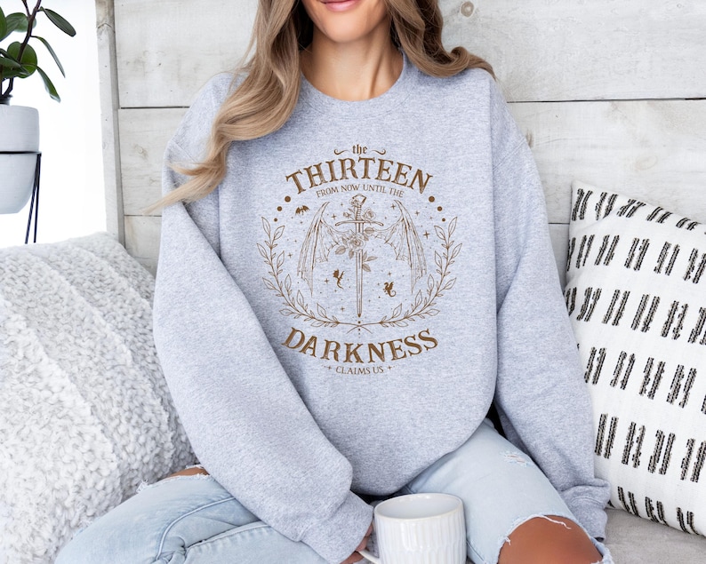 May include: A gray sweatshirt with a graphic design featuring a sword and wings with the text "the thirteen from now until the darkness claims us".