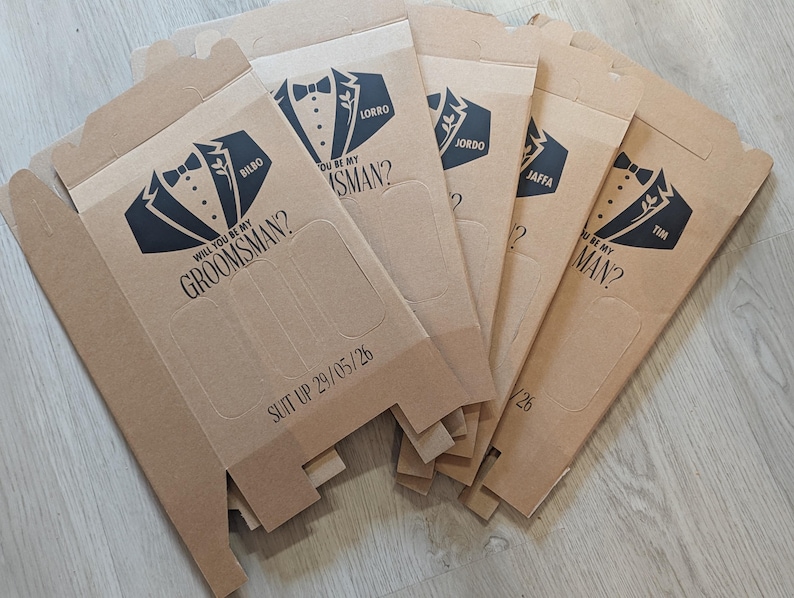 May include: Five brown cardboard boxes with a tuxedo graphic and the text "Will you be my groomsman?" and "Suit up 29/05/26".