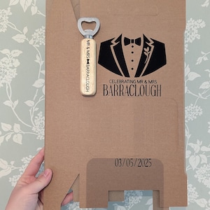 May include: A brown cardboard box with a black tuxedo graphic and the text "Celebrating Mr. & Mrs. BARRACLOUGH 03/05/2025". A wooden bottle opener with the text "Mr. & Mrs. BARRACLOUGH" is included.